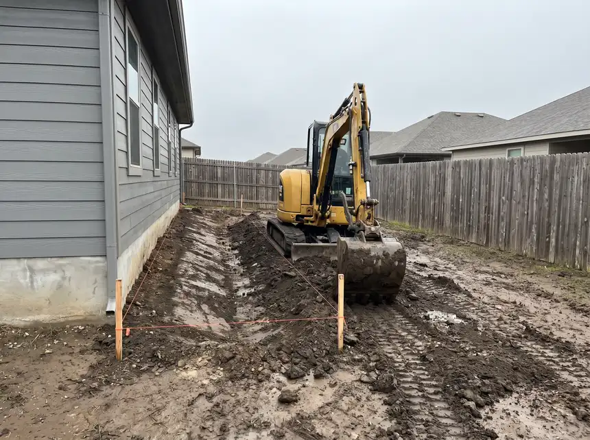 A compact excavator regrading a residential back yard toward a swale in Saskatoon, SK